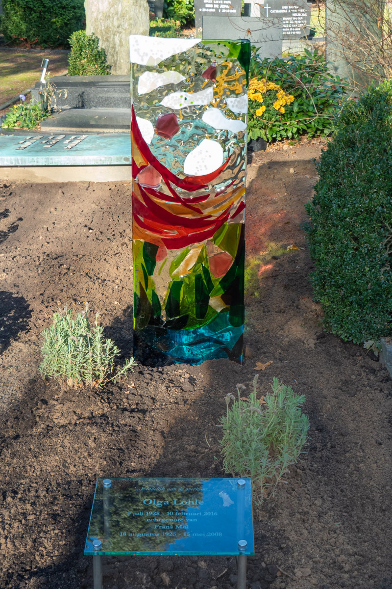 Glazen grafmonument in rood, groen en blauw op een begraafplaats
